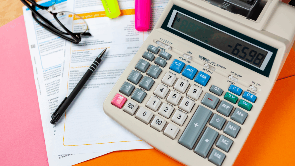 Calculator and printed pricing comparison sheet on a desk representing evaluation of PG management software pricing options.