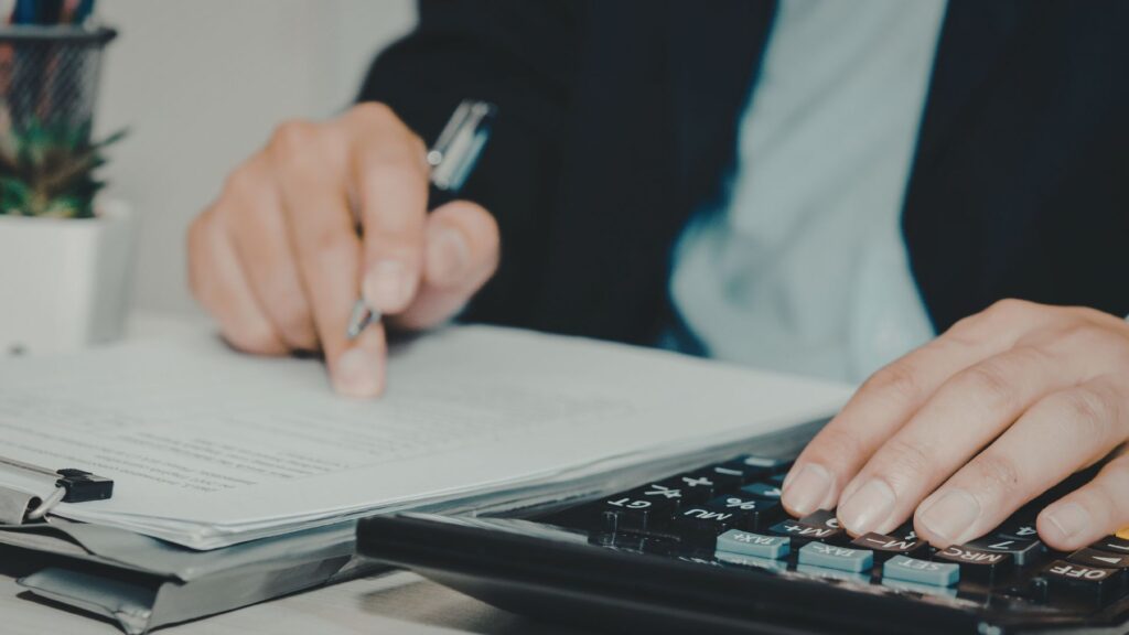 Person working with a calculator and documents on a desk, manually calculating and managing records, with a calculator placed beside them.