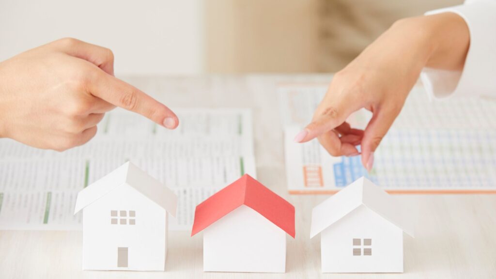 Real estate property comparison concept with hands pointing at house models, representing real estate property management software and decision-making.